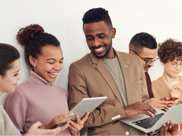 Lumina - Tile Image - A group of mixed race people dressed in neutral clothing smiling and looking at laptops and tablets